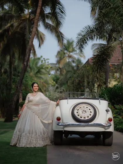 A touch of vintage charm for a Goa wedding, with the bride posing next to a classic car amidst the palm trees.