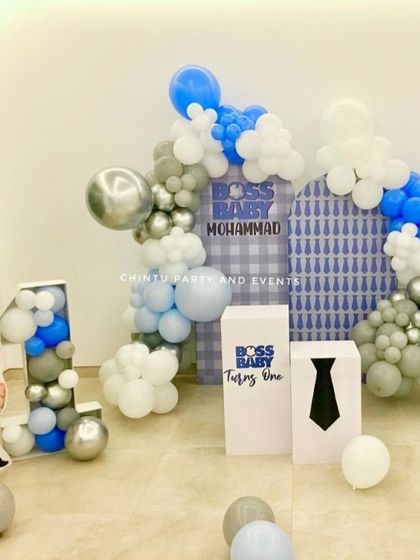 A sharp Boss Baby themed first birthday decoration. The setup uses blue, white, and silver balloons, themed pedestals, and a large '1' marquee filled with balloons.