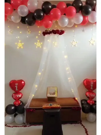 For a truly romantic gesture, I can create an intimate canopy setup in your room. This one includes a sheer curtain with fairy lights, a ceiling garland of red and black balloons, and special 'I love you' heart-shaped foil balloons.