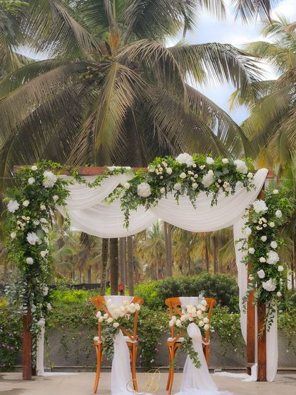 A minimalist wedding altar featuring a simple wooden frame, elegantly draped with flowing white fabric and adorned with asymmetrical arrangements of white flowers and greenery.