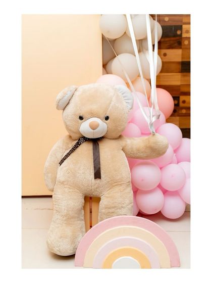 A large, soft teddy bear prop holding balloons, next to a pastel rainbow, adding a touch of sweetness to the decor.