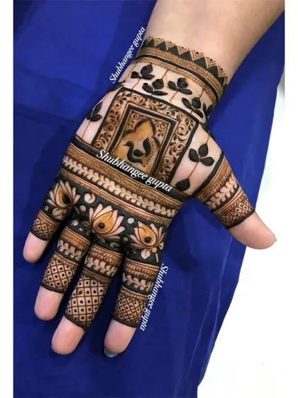 A designer back-of-hand mehndi with a central Ganesh motif. The surrounding patterns are kept simple and clean, making the central figure the main focus.