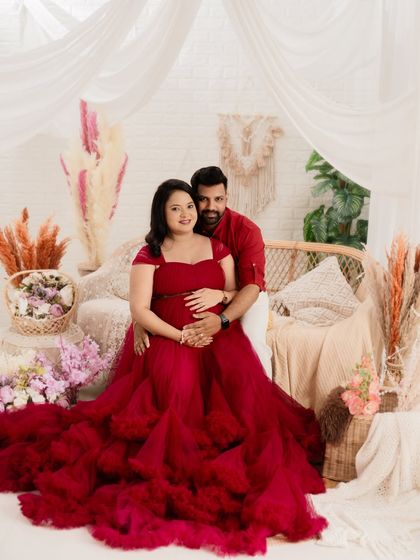 A classic couple portrait in our boho studio set. The partner embraces the mom-to-be, who is radiant in a stunning red gown, creating a beautiful and romantic image.