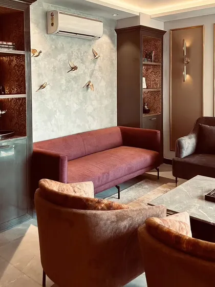 A wider view of a living room where multiple textures coexist harmoniously. A textured paint surface with decorative bird motifs, a plush maroon sofa, and a high-gloss display cabinet come together to create a rich, tactile environment.