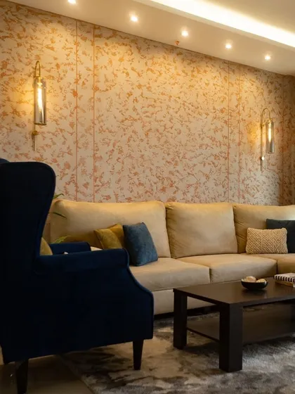A cozy corner of a living room, where a plush navy blue wingback chair adds a pop of color. The textured wall and warm ambient lighting create the perfect spot to relax with a book.