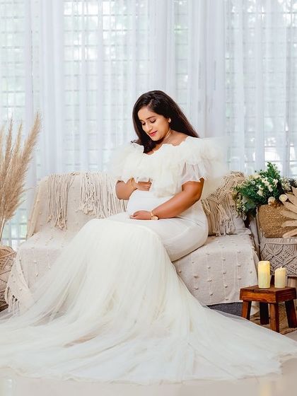 A quiet, contemplative portrait of the mother-to-be looking down at her bump. The soft light from the window and the dreamy decor create a peaceful mood.