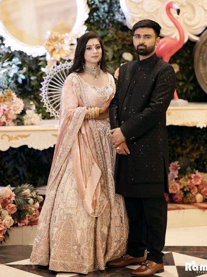 A classic portrait of the couple at their engagement, standing before an ornate backdrop. Their elegant pastel and black outfits create a sophisticated look.