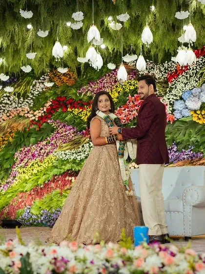 A breathtaking reception stage featuring a massive wall of multi-colored fresh flowers. The sheer scale and artistry of this floral backdrop create a vibrant, unforgettable setting for the couple's big day.