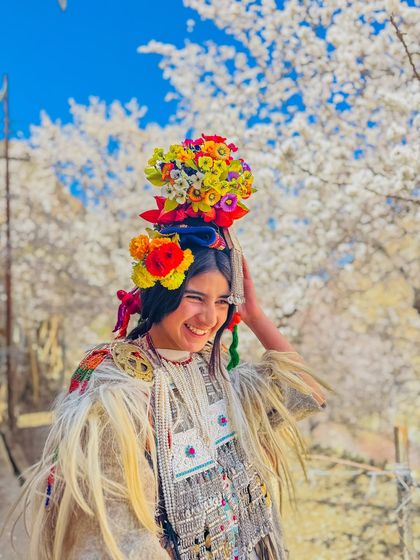 A vibrant portrait of a smiling Brokpa woman in Ladakh. Her traditional attire, adorned with flowers and silver, is a beautiful expression of her unique cultural heritage.