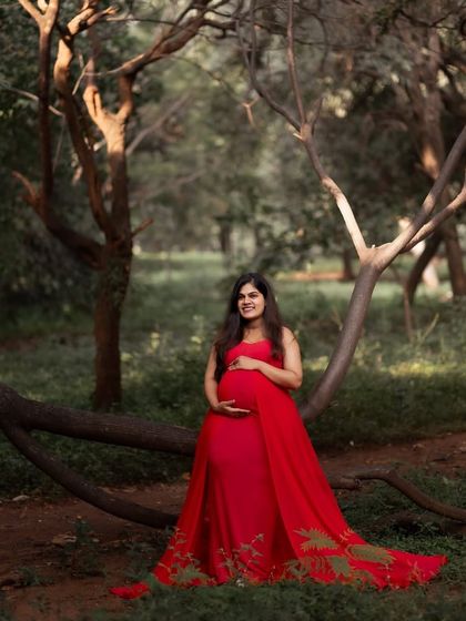 Our Rosie gown in a beautiful forest setting. The vibrant red stands out beautifully against the green foliage, and the embroidered trail adds a unique touch.