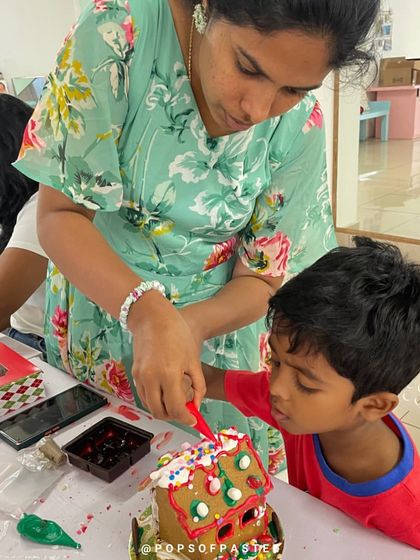 A mother and son add sprinkles and candies to their gingerbread house, bringing it to life with color and texture.