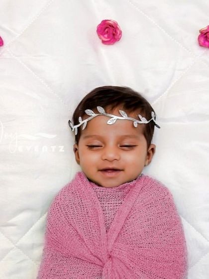Simplicity at its finest. A newborn baby girl is swaddled in a soft pink wrap, wearing a delicate silver leaf headband on a clean white, quilted background. This pristine theme focuses entirely on your baby's peaceful expression.