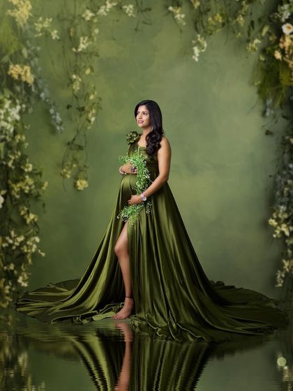 This fine art portrait that looks like a painting. The mother-to-be stands like a forest nymph in a green gown, surrounded by hanging vines and a water reflection.