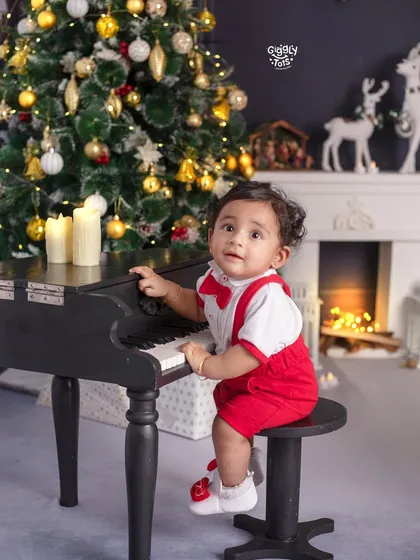 This little musician is ready to play some Christmas carols on his mini piano, dressed in a festive red outfit.