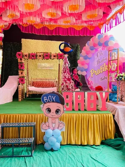 The main stage of a baby shower featuring a moon prop, a decorated swing, and Radha-Krishna cutouts.