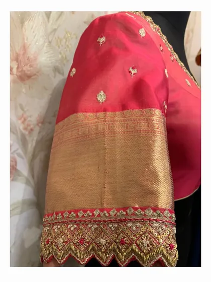 A close-up of a red silk sleeve with a cutwork border. The intricate design is created using zardosi and thread embroidery.