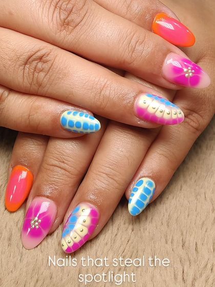 Nails that steal the spotlight. This vibrant and eclectic set features a mix of neon orange, airbrushed pink florals, and a unique blue and yellow textured design, all accented with tiny gold studs.