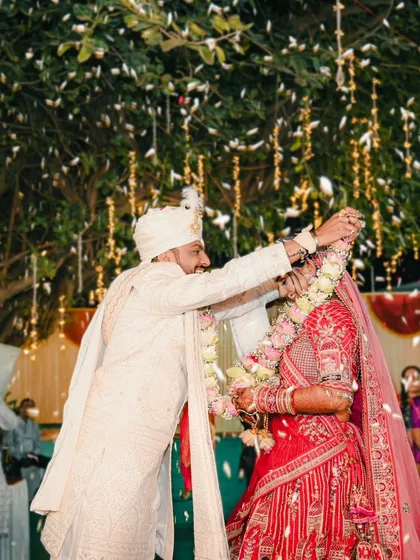 A close up of the groom placing the garland on the bride during the varmala ceremony, captured amidst a shower of petals.