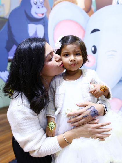 A mother gives her daughter a kiss on the cheek. The jungle-themed temporary tattoos on their hands are a fun detail that adds to the theme.
