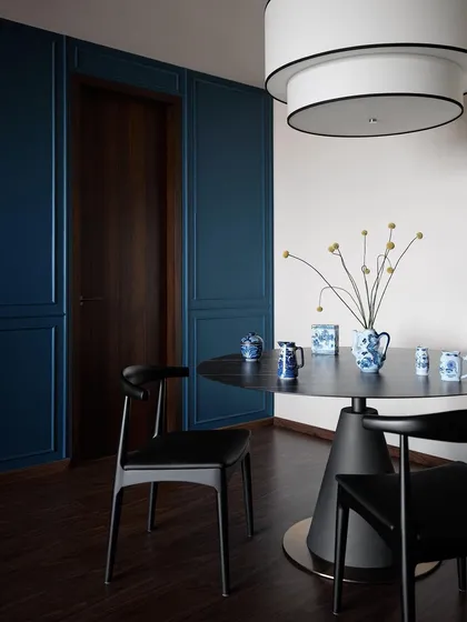 A moody and intimate dining corner in the Peninsula Residence. The deep blue panelled walls create a dramatic backdrop for the minimalist black dining set and a collection of the client's blue and white antique ceramics.