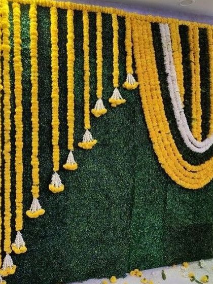 A classic Haldi backdrop featuring a green wall adorned with beautiful marigold flower garlands.