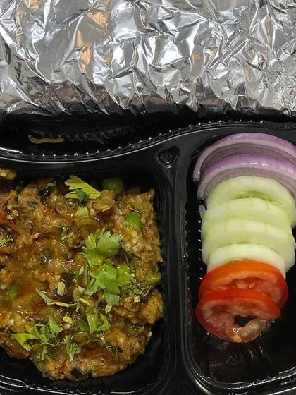 This tiffin features a home-style Baingan Bharta, a smoky roasted eggplant mash cooked with spices. It comes with fresh salad and rotis, offering a rustic and flavorful meal.