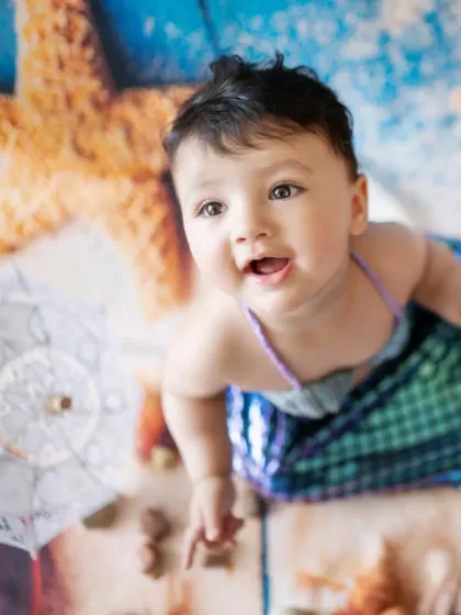 A cute baby dressed as a mermaid for a unique milestone photoshoot. The backdrop and props create an enchanting under-the-sea world.