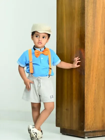 A little boy posing confidently by a wooden pillar in an outdoor setting.