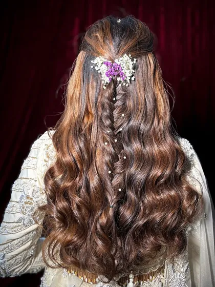 The hairstyle featured a center-parted, half-up style with soft waves, adorned with a fishtail braid and delicate flowers.