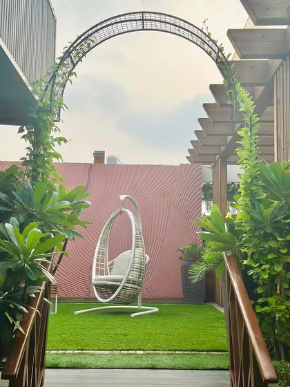 A perfect urban retreat designed by our team. This terrace features a lush artificial lawn, a climbing vine archway, and a comfortable swing chair, offering a peaceful garden view against the city skyline.