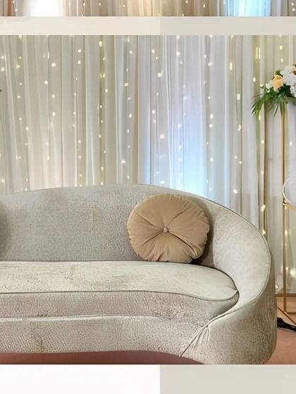 Minimalist decor at its finest. A sleek, curved sofa is complemented by a simple floral arrangement and a backdrop of twinkling fairy lights for a touch of quiet elegance.