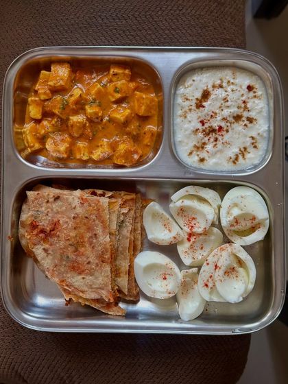 This plate features a high-protein combination of paneer curry with methi paratha, boiled egg whites, and a side of raita.