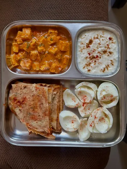 A delicious meal of paneer paratha, paneer curry, curd, and boiled egg whites. This plate is packed with protein from both dairy and eggs.
