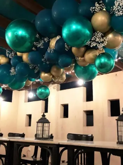 A ceiling installation of teal and gold balloons mixed with delicate baby's breath. This is a great way to add drama and a festive feel to a restaurant or banquet hall space for a party.