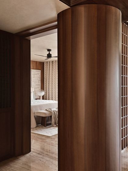 A glimpse into a bedroom through a curved, wood-paneled entryway. This architectural detail creates a sense of discovery and adds a soft, organic feel to the transition between spaces.