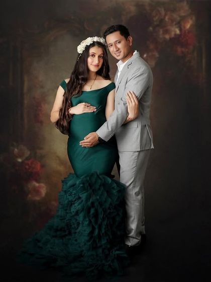 A life giving birth to another life. This couple stands together in a loving embrace, framed by a dark, romantic floral backdrop that enhances the magical feeling.