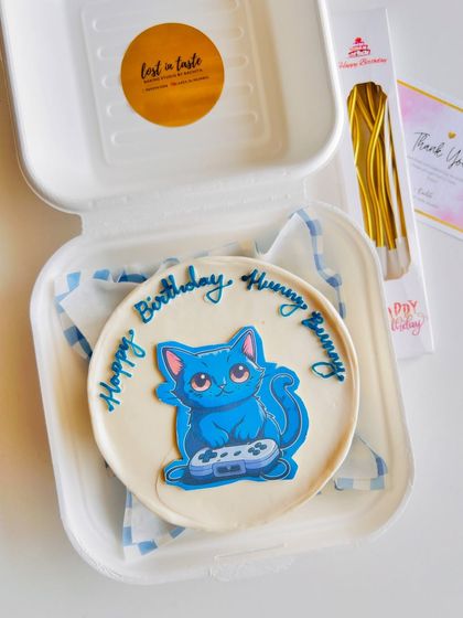 A custom bento cake for a gamer, featuring a cute blue cat holding a controller. It's a great way to combine a hobby with a sweet celebration.