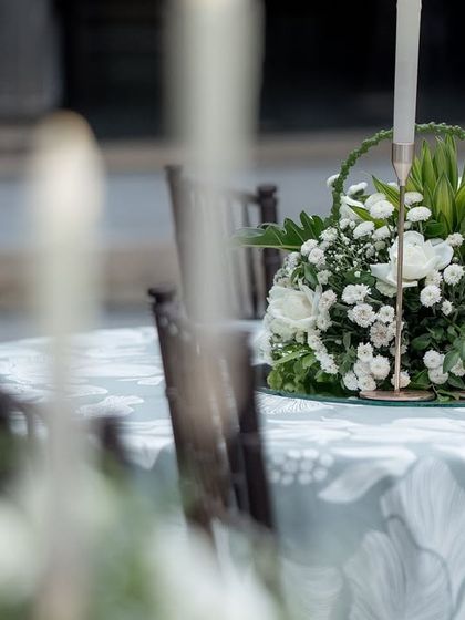 A floral centerpiece with white roses and candles on a table set for a reception, showcasing elegant table decor.