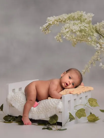 We use a variety of creative props to bring a touch of whimsy to our sessions. Here, a newborn rests peacefully on a miniature white bed, surrounded by delicate flowers for a dreamy, artistic portrait.