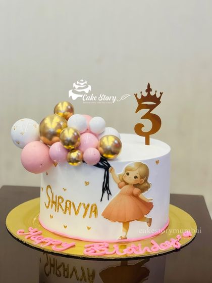 An elegant cake for Shravya's third birthday. This design features a lovely illustration of a girl holding balloons, with a real bunch of pink, white, and gold balloons on the cake.