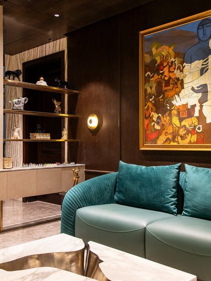 A lounge area in 'The Outhouse' project, featuring a deep blue sofa and a striking marble coffee table. The space is designed to be moody and luxurious, with bold art and rich textures.