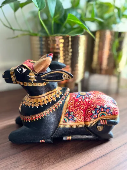 This seated Nandi sculpture carries a quiet, regal presence. The deep black base is illuminated by intricate red and gold patterns, a combination that feels both timeless and powerful, making it a substantial piece for a table or shelf.