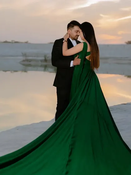 A close, romantic embrace at the water's edge. The long green gown pools around the couple, creating a beautiful and dramatic base for the portrait.