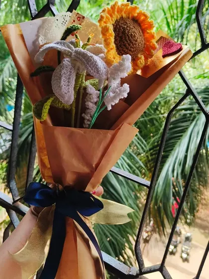 A lovely bouquet featuring a bright crochet sunflower and elegant white lilies, tied with a beautiful blue and gold ribbon.