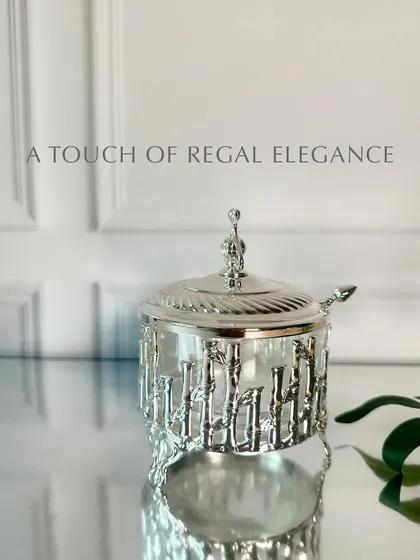 A charming glass sugar pot with intricate silver-plated bamboo engravings. Paired with a delicate spoon, it is perfect for adding a touch of sweetness and style to your table.