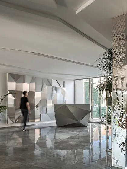 The main reception area of the Stainless Steel Office features an angular, custom-designed stainless steel desk set against a matching feature wall, creating a cohesive and modern first impression.