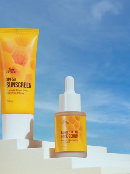 A honey-based sunscreen and serum duo, shot against a bright blue sky. This setup communicates sun protection and a fresh, airy feel.