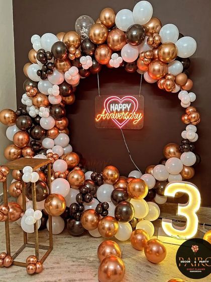 A chic 3rd-anniversary ring decoration with a full arch of metallic bronze, black, and white balloons, a neon sign, and a "3" marquee number.