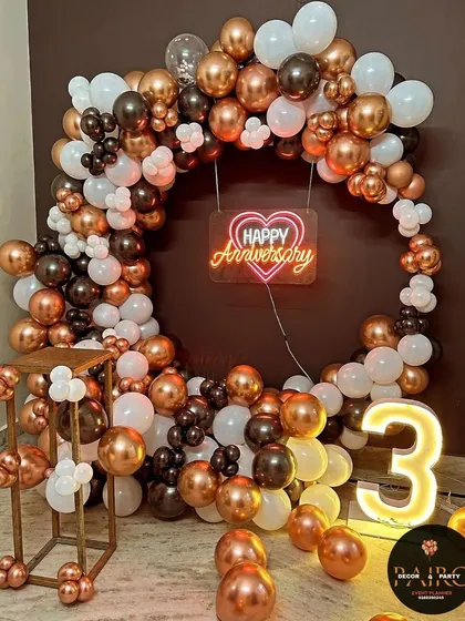 A chic 3rd-anniversary ring decoration with a full arch of metallic bronze, black, and white balloons, a neon sign, and a "3" marquee number.