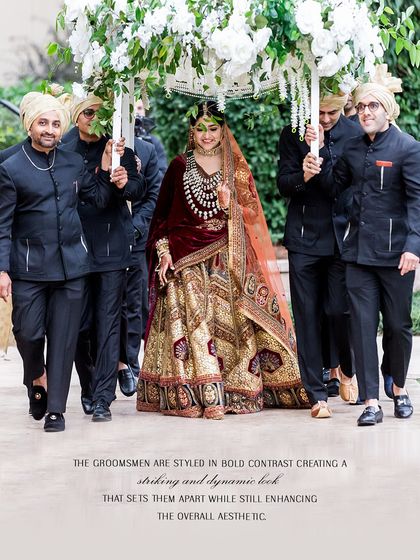 The bride's grand entrance, a moment of pure heritage and emotion. We styled her in a magnificent red and gold lehenga, rich with traditional embroidery. The groomsmen, dressed in contrasting black bandhgalas, create a striking and dynamic frame, enhancing the bride's regal presence.